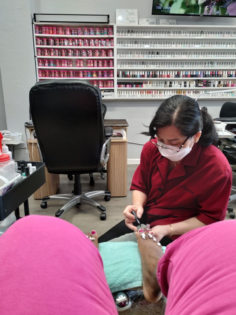A nail technician giving a pedicure at Nancy’s Salon, in front of the polish wall
